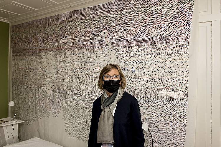 Ana Holenstein-Wyrsch steht im elterlichen Schlafzimmer der Ausstellung vor einem Textilwerk ihrer Mutter Gertrud Guyer Wyrsch.